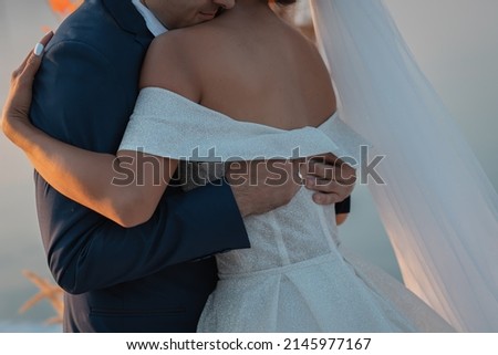 Loving couple at an international wedding at sunset. Beautiful sophisticated bride of Asian appearance. Strong manly groom of Caucasian appearance. Mixed marriages. Warm embrace. Royalty-Free Stock Photo #2145977167