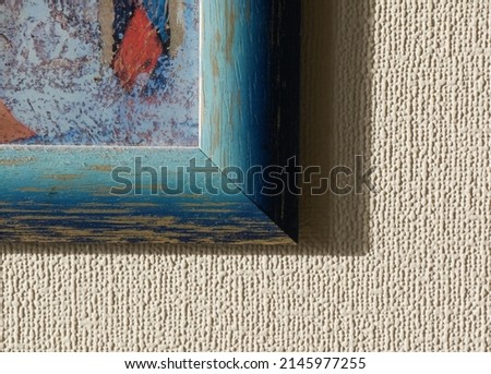 Fragment of old dusty wooden frame with scratches and cracks and abstract multicolored image inside it. Light blurred textured surface with shadow from frame. Focus on foreground. Sun flares.
