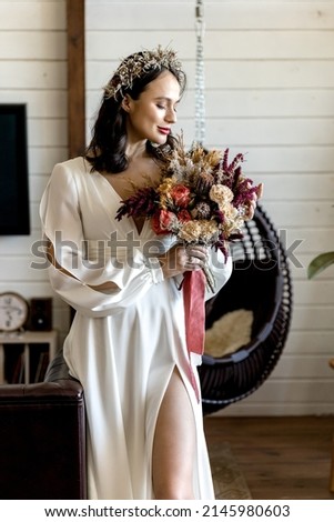 Beautiful cute bride in a chic white dress with a bouquet in her hands in the apartment. High quality photo