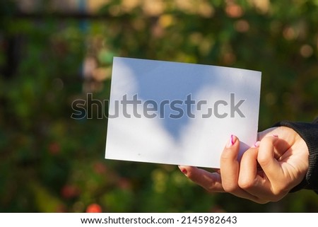 A woman's hand with a white blank sheet of paper outdoors on a green nature background. Copy space for the text . Protester activist. Paper in hand against a background of blurred green foliage.