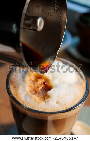 Freshly brewed espresso is poured from a machine into a glass with milk froth.
