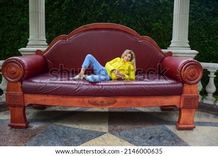 On a vintage soft giant couch for the scenery of one-time work, a young blonde woman lies and smiles