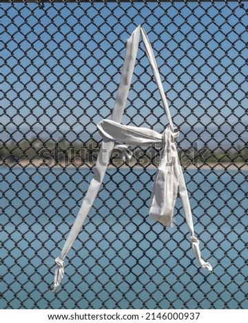 A white letter A, made out of cloth, is tied to a chain link fence.