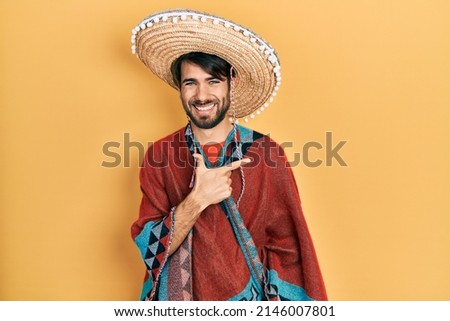 Young hispanic man holding mexican hat cheerful with a smile of face pointing with hand and finger up to the side with happy and natural expression on face 
