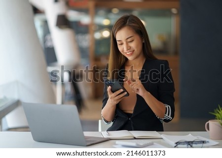 Charming young Asian business woman with a smile sitting using smartphone at the office.