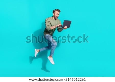 Full length photo of millennial blond guy jump type laptop wear sweater jeans shoes isolated on turquoise background
