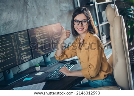 Portrait of beautiful cheery girl expert developing web project showing thumbup at workplace workstation indoors