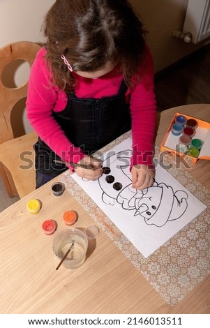 little girl draws snowman on paper with paints, in pink sweater, paint, water, in the room, drawing on white paper, education, drawing lesson