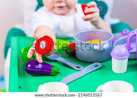 Blurred little child holding a toy vegetable in his hands on the background of dishes.
