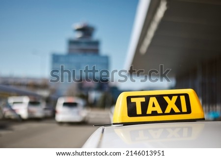 Selective focus on taxi sign on roof of car against airport terminal. 

