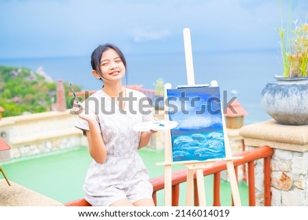Young girl using brush drawing picture on canvas paper, at beautiful landscape view at koh tao Thailand.