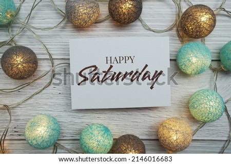 Happy Saturday text on paper card with LED cotton balls top view on wooden background