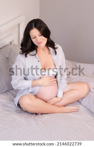 charming pregnant woman in shirt on bed. happy pregnancy.