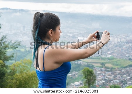 beautiful latin woman on top of a colombian mountain taking a picture of the beautiful landscape of the city of Pereira. blue haired girl taking a selfie on a cold morning.