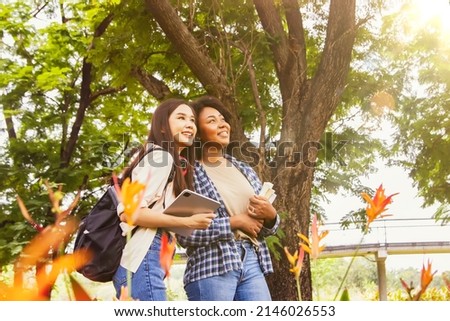 Portrait two ethnic female students young people carrying backpacks and learning supplies are happy intimacy walk in nature study garden admire the beauty of nature show their happy faces and eyes.