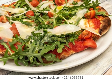 Detail of a delicious pizza, with Parmesan cheese shavings, arugula in abundance, pomodoro sauce and chopped cherry tomatoes with Spanish olive oil