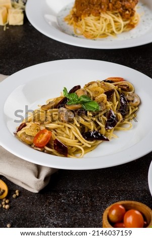 a cooked pasta spaghetti  with mushroom sauce, slice beef, olive oil and fresh green parsley in white oval plate with ingredients on black background