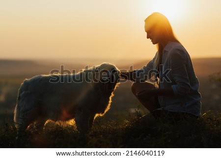 Silhouette of happy woman playing with her dog at sunset on the field.