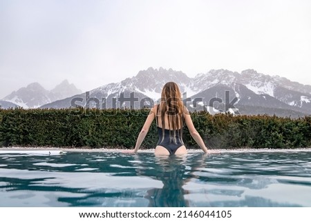 Rear view of tourist swimming in hot pool during winter. Woman in swimwear looking at snowcapped mountains. She is relaxing in luxurious hotel. Royalty-Free Stock Photo #2146044105
