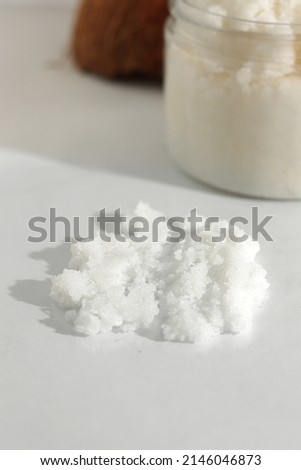 Scattered scrub, jar, coconut on white background. Home spa treatment concept, organic cosmetic. Vertical photo.