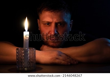 A man sits in the dark with a candle at the table.