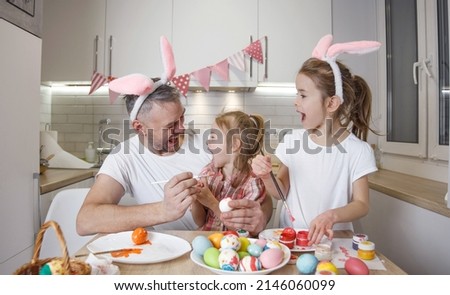 a happy father with two young daughters are laughing and dabbling, painting Easter eggs and preparing for the Easter holiday. Preparation for the Easter holiday.