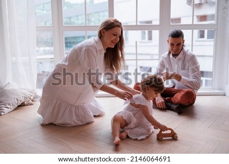 Cute family of father, mother and daughter smiling, playing and joking together. Family playing at window with toy, girl flying