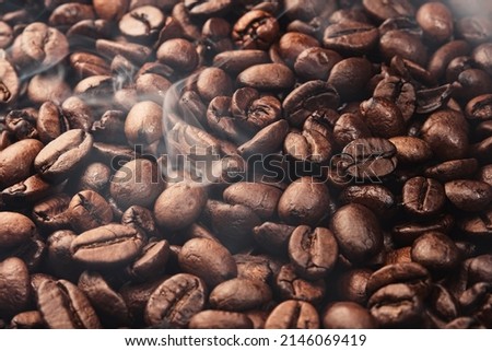 Texture of freshly roasted, ready-to-drink coffee, steam rising over the beans. Close-up, selective focus. Scene of coffee beans. Black ground coffee