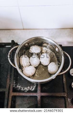 Chicken white large eggs are boiled in boiling water in an old metal pan on the stove in the kitchen. Morning breakfast, food photography, concept.