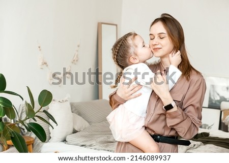 A little girl kisses her mother on the cheek at home in a modern bright bedroom. The concept of parenthood, love and care
