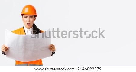 Frustrated and displeased female asian engineer, chief architect at construction zone, looking disappointed after studying blueprints, stare camera, scolding manager, white background