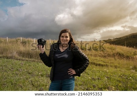 Beautiful Hispanic woman photographer with her camera in her hand happy posing in the middle of the field on a cloudy afternoon