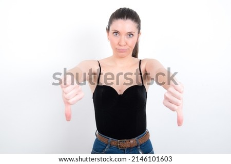young caucasian girl wearing tank top over white background being upset showing thumb down with two hands. Dislike concept.