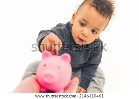 Adorable baby boy using pink piggy bank by putting coins there. Future and savings concept. Studio shot over white background. High quality photo