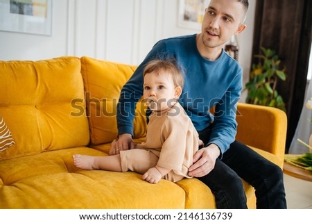 child with a pacifier sitting on a yellow sofa with his father. High quality photo