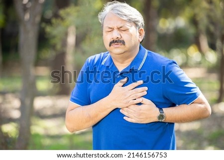 Senior Indian asian male presses hand to his chest as he is suffering from bad pain or heart attack at park outdoor, old people heart disease problem, healthcare concept. Royalty-Free Stock Photo #2146156753