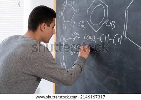 hand of arabic chemistry teacher with chalk drawing formulas and elements, signs and symbols of chemistry, chemist education concept on blackboard