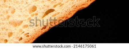 slice of white bread close up isolated on a black background. rough textured surface chopped piece loaf of natural organic food with holes. top view. abstract concept of the planet and space. banner
