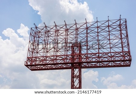 A view of an old sign, a red steel structure towering in anticipation of an advertisement with clouds in the sky as a backdrop during the day. Royalty-Free Stock Photo #2146177419