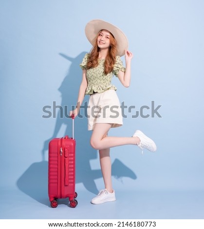 Full length image of young Asian girl with suitcase on blue background, travel concept