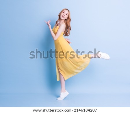 Full length image of young Asian woman wearing yellow dress on blue background
