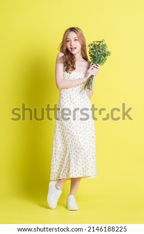 Image of young Asian woman holding flowers on yellow background