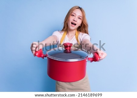 Image of young Asian woman holding pot on blue background