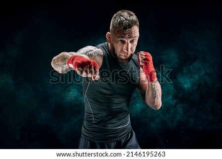 Kickboxer in red bandages is boxing against a background of smoke. The concept of mixed martial arts. MMA