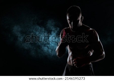 Kickboxer in red bandages poses against a background of smoke. The concept of mixed martial arts. MMA Royalty-Free Stock Photo #2146195273