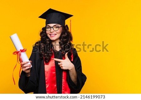 Girl graduate in graduation hat and eyewear with diploma on yellow backdrop. Brunette young woman wearing graduation cap and ceremony robe holding Certificate tied with red ribbon. Education Concept  Royalty-Free Stock Photo #2146199073