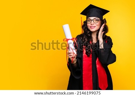 Pleased young woman graduate in graduation hat and eyewear with diploma on yellow wall. Smart female best student wearing graduation cap and ceremony robe holding Certificate. Education Concept  Royalty-Free Stock Photo #2146199075