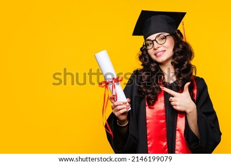 Girl graduate in graduation hat and eyewear with diploma on yellow backdrop. Brunette young woman wearing graduation cap and ceremony robe holding Certificate tied with red ribbon. Education Concept  Royalty-Free Stock Photo #2146199079