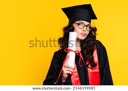 Girl graduate in graduation hat and eyewear with diploma on yellow backdrop. Brunette young woman wearing graduation cap and ceremony robe holding Certificate tied with red ribbon. Education Concept  Royalty-Free Stock Photo #2146199081