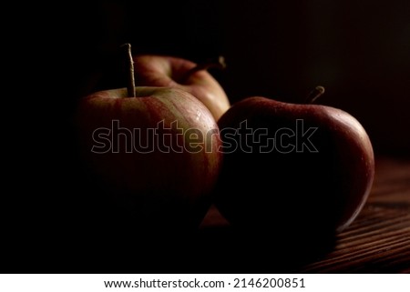 Apples in the dark. Low-key picture of three apples on a wooden table. Still-life studio shot.